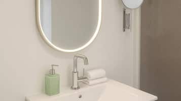 Une salle de bain moderne avec un lavabo blanc, un miroir doté d’un cadre lumineux, un distributeur de savon et un porte-serviettes.