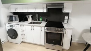 A compact kitchen with white cabinets, a microwave, a coffee maker, a sink, a stove, and a washing machine.