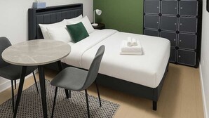 A hotel room with a bed, a bedside table, two chairs, a small table, a nightstand, and a wardrobe.
