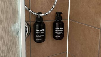 Une salle de bain avec deux bouteilles noires étiquetées « SHAMPOO » et « GEL DOUCHE » posées sur un mur carrelé.