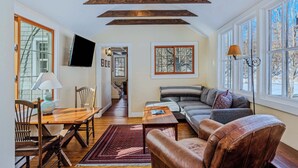 A living room with a wooden ceiling, a sofa, a coffee table, and a TV mounted on the wall. - Riverside Cottage on the Ottauquechee River (Woodstock)