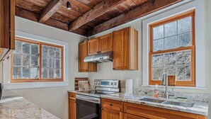 A kitchen with wooden cabinets, a stainless steel range, and a window with frosted glass. - Riverside Cottage on the Ottauquechee River (Woodstock)