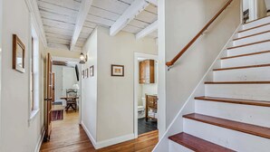 A wooden staircase leading to a second floor, a hallway with wooden flooring, and a dining area with a table and chairs. - Riverside Cottage on the Ottauquechee River (Woodstock)
