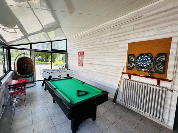 Een biljart, een hangstoel en een dartbord in een kamer met een groot raam.