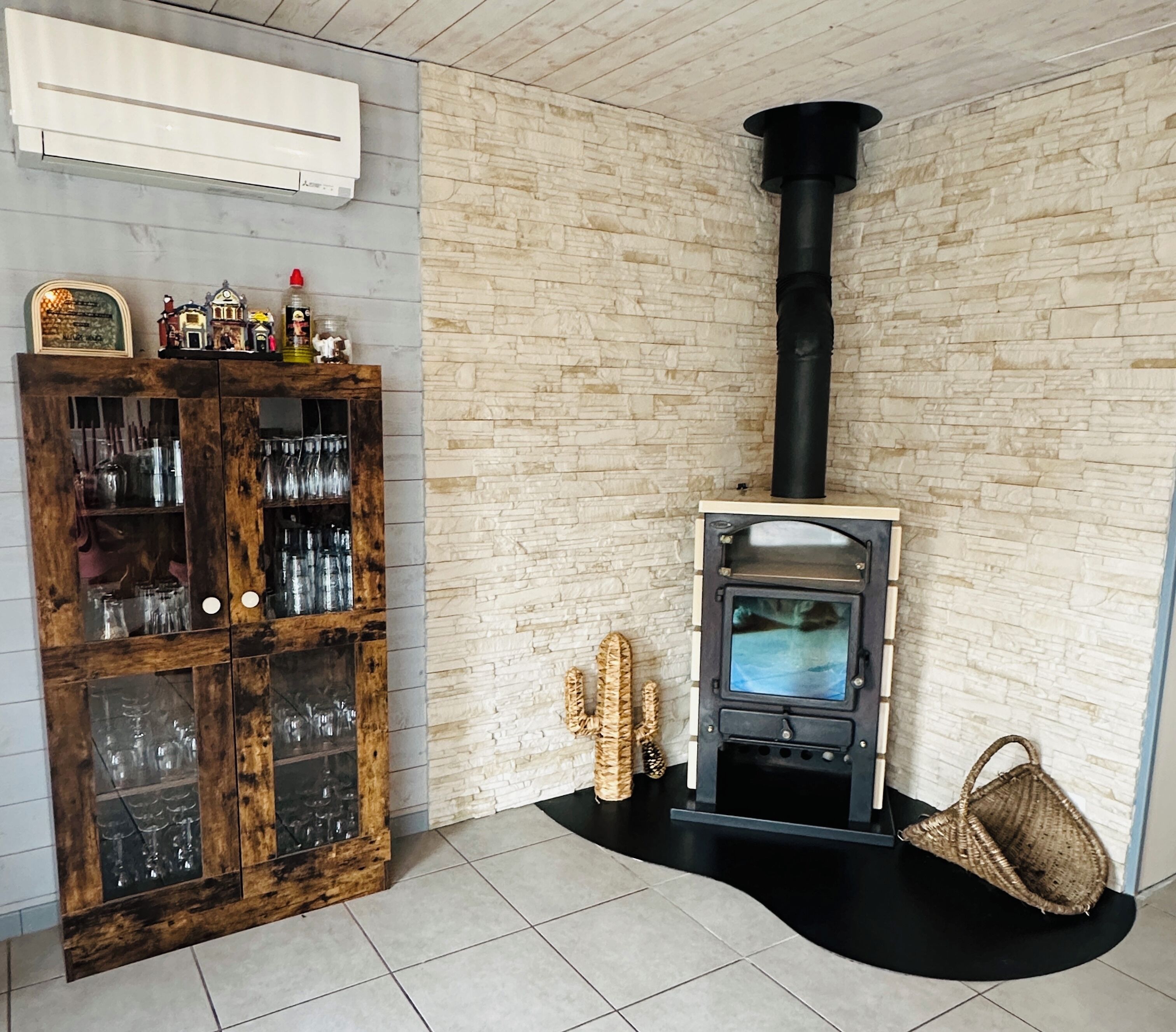 A room with a stone wall, a wooden cabinet with glass doors, a black stove, and a woven basket.