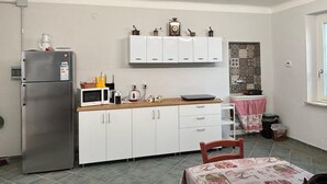 Una cocina compacta con armarios blancos, un refrigerador de acero inoxidable, un microondas y una pequeña mesa.