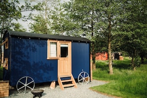 A small blue metal shed with a wooden door, a window, and two large wheels at the base.