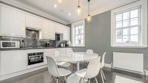A modern kitchen with white cabinets, a marble countertop, and a dining area with a round table and white chairs.