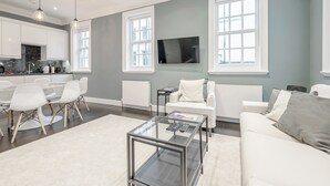 A modern living room with a glass coffee table, white sofas, and a dining area with a glass table and chairs.