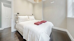 A bedroom with a bed, white walls, a ceiling light, and a door.