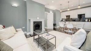 A modern living room with a glass coffee table, white sofas, and a fireplace.