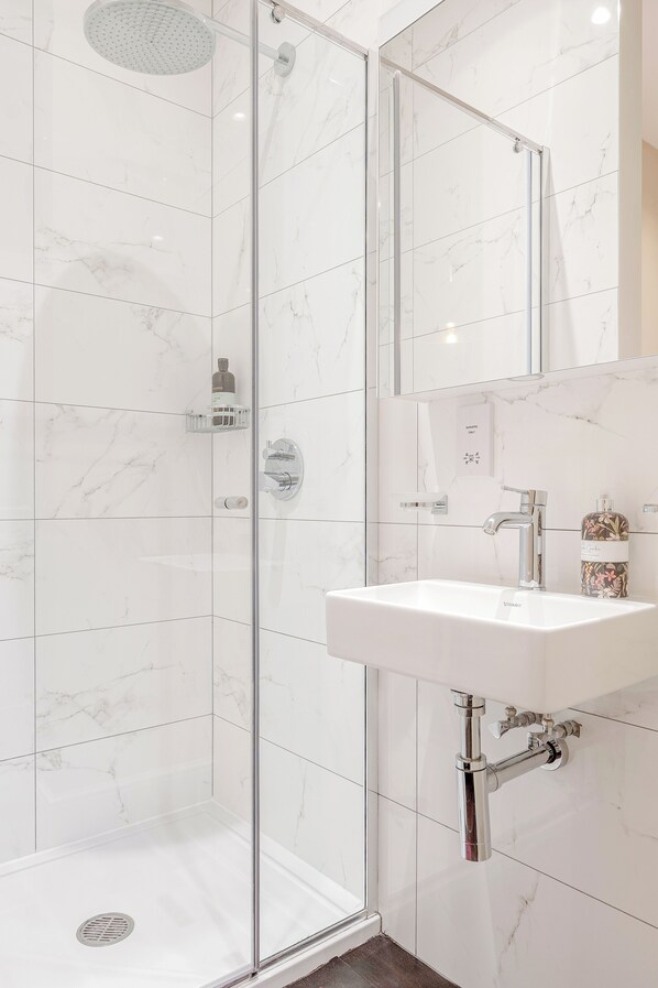 A modern bathroom with a glass-enclosed shower, a white sink, and a marble-tiled wall.