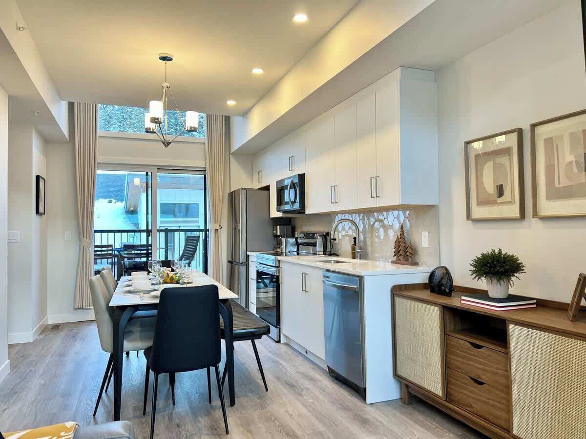 A modern kitchen with white cabinets, stainless steel appliances, and a dining area with a table and chairs.