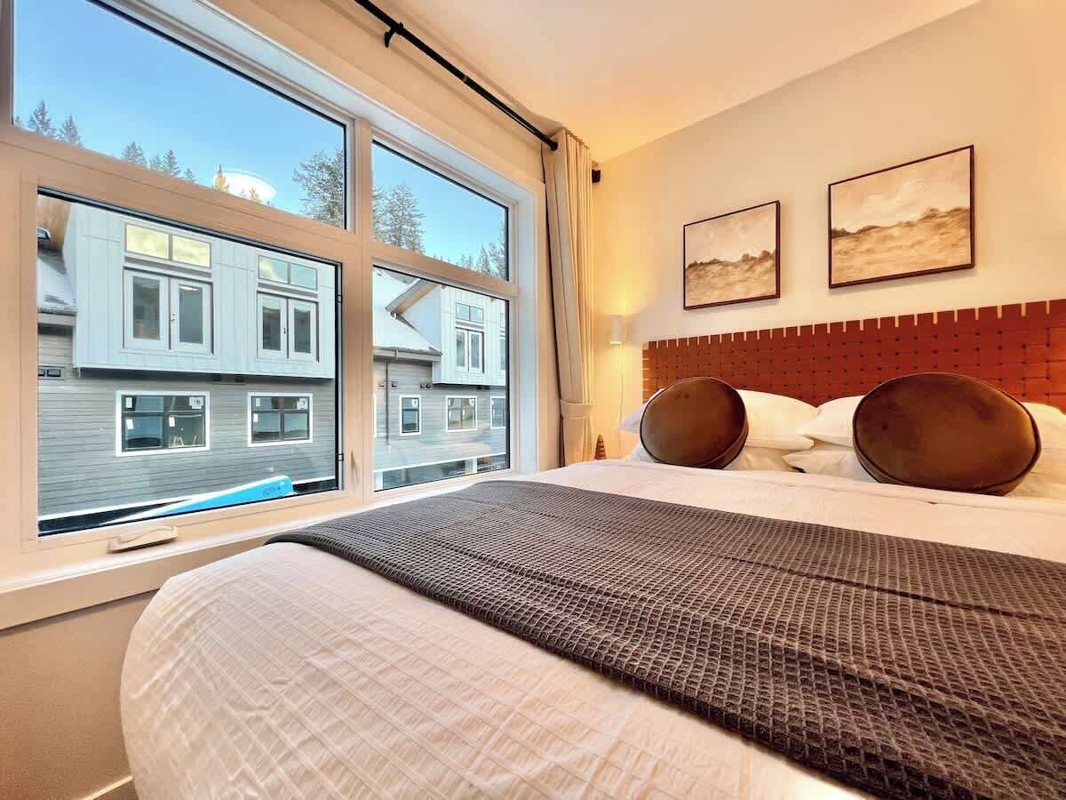 A hotel room with a large bed, a window with a view of buildings, and two framed pictures on the wall.