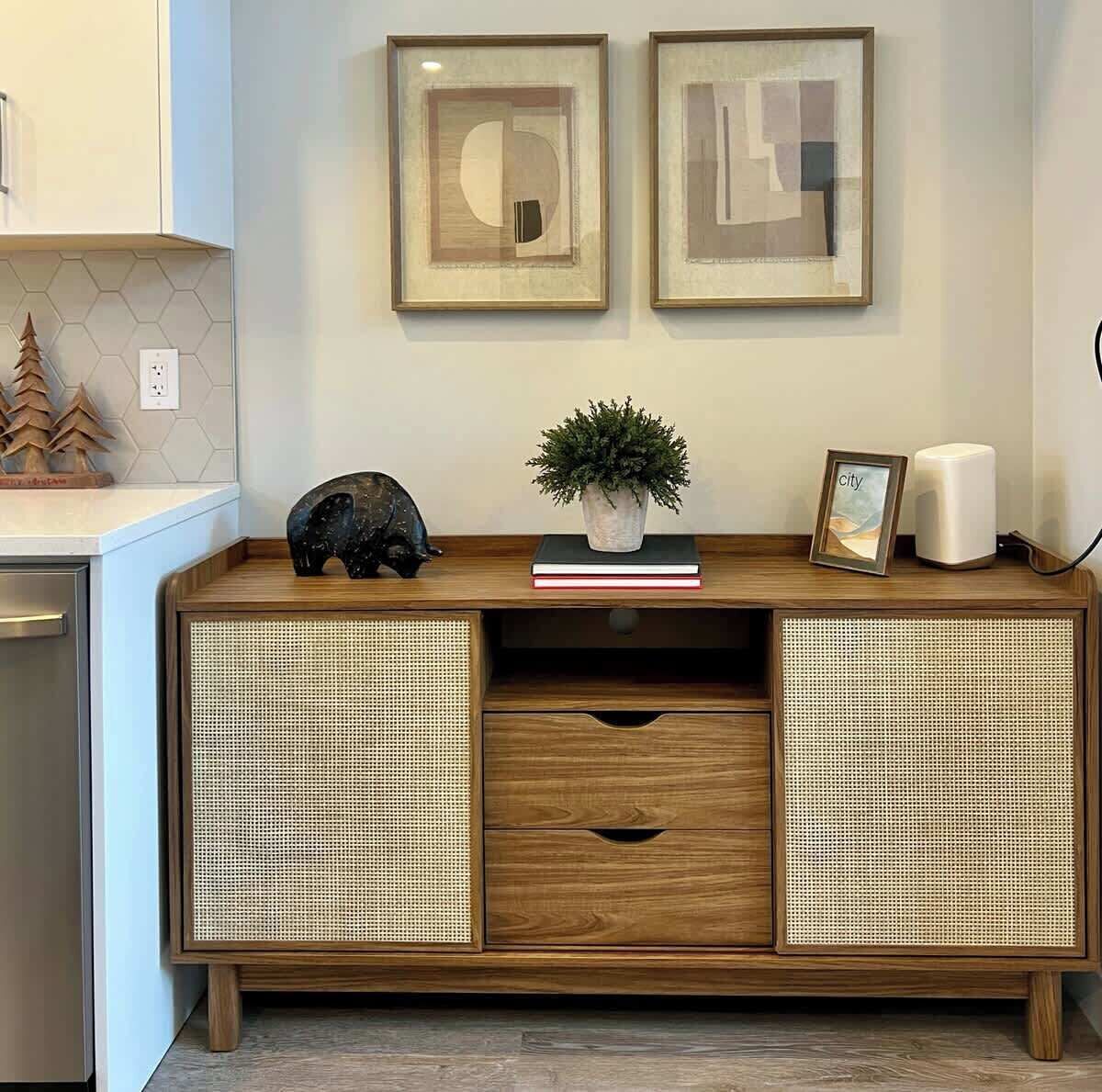 A wooden console with woven panels, a small plant, a framed picture, and a piggy bank on a kitchen counter.