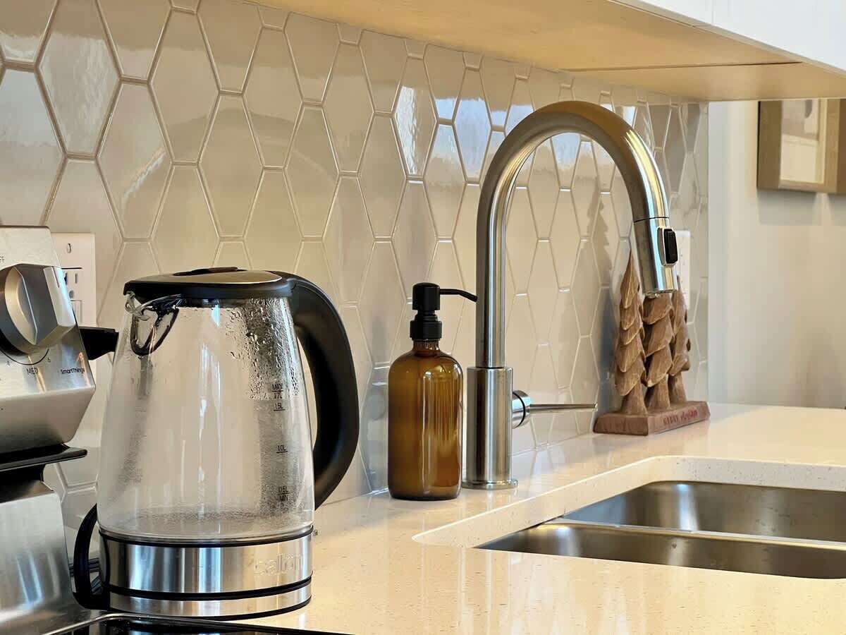 A kitchen with a modern design, featuring a stainless steel kettle, a soap dispenser, and a unique wooden soap dish.