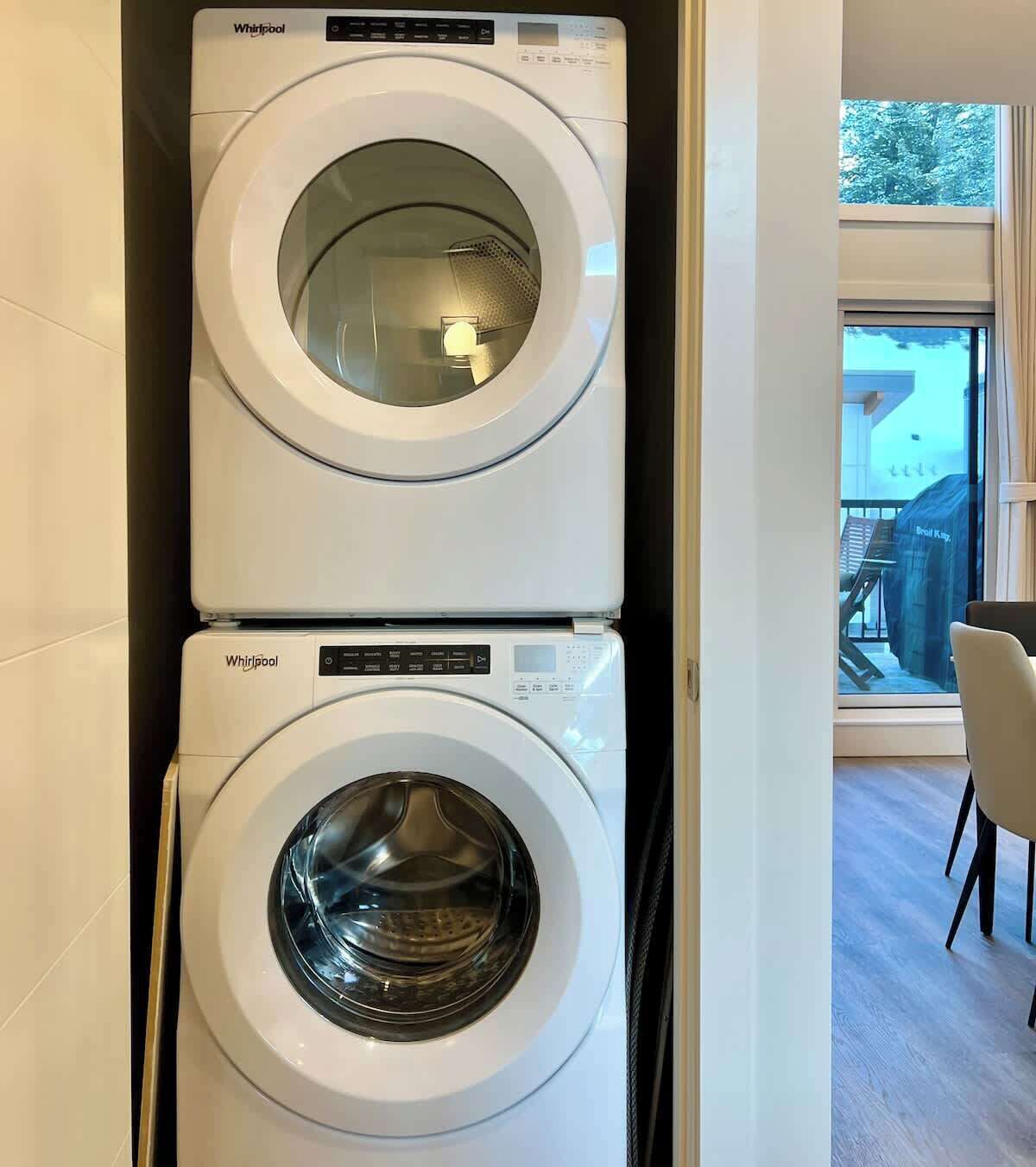 Un appareil combiné lave-linge et sèche-linge, installé en hauteur, dans une cuisine moderne avec vue sur un balcon et un espace salon extérieur.