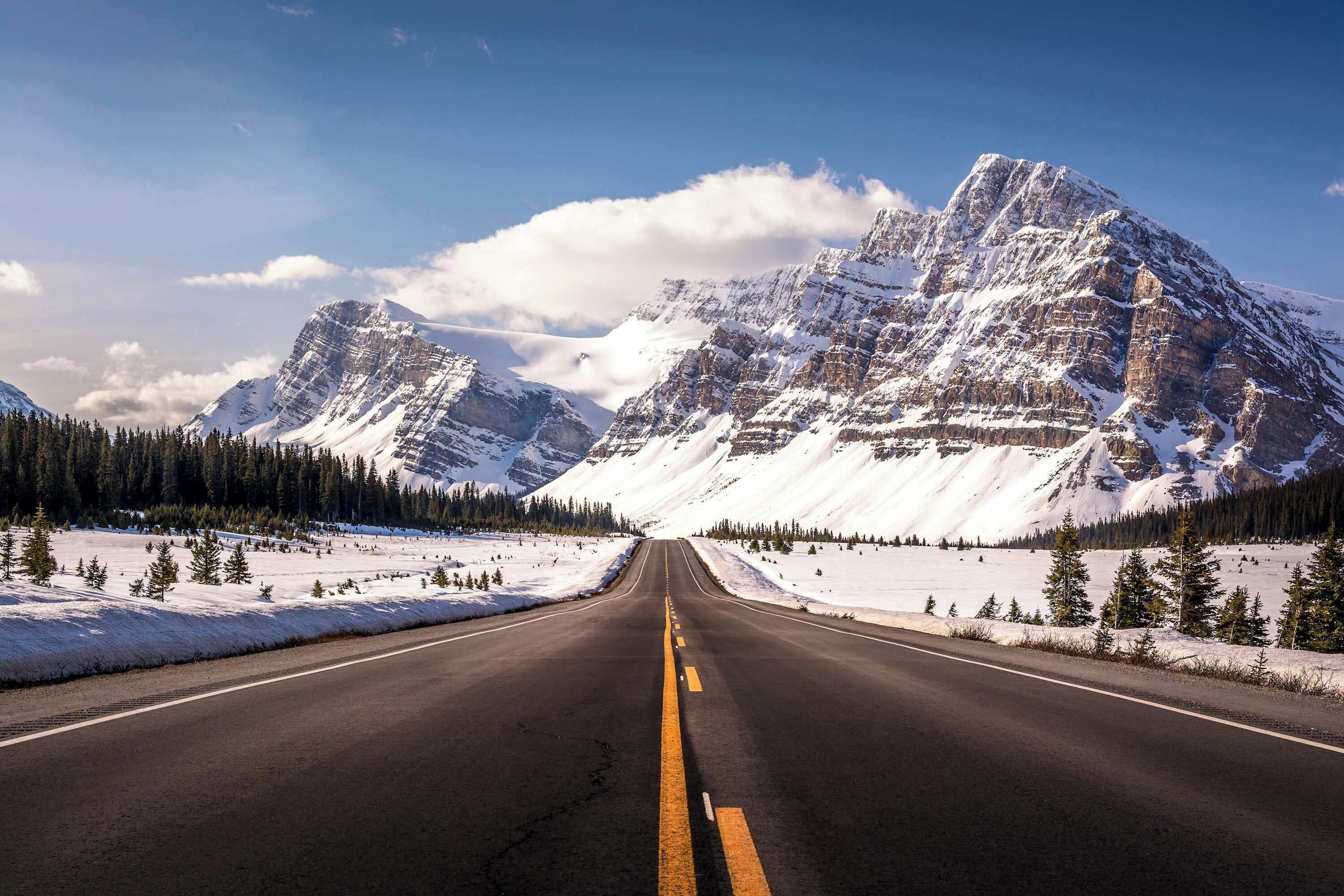 A road leading to a mountain range with snow-covered peaks and a clear sky.