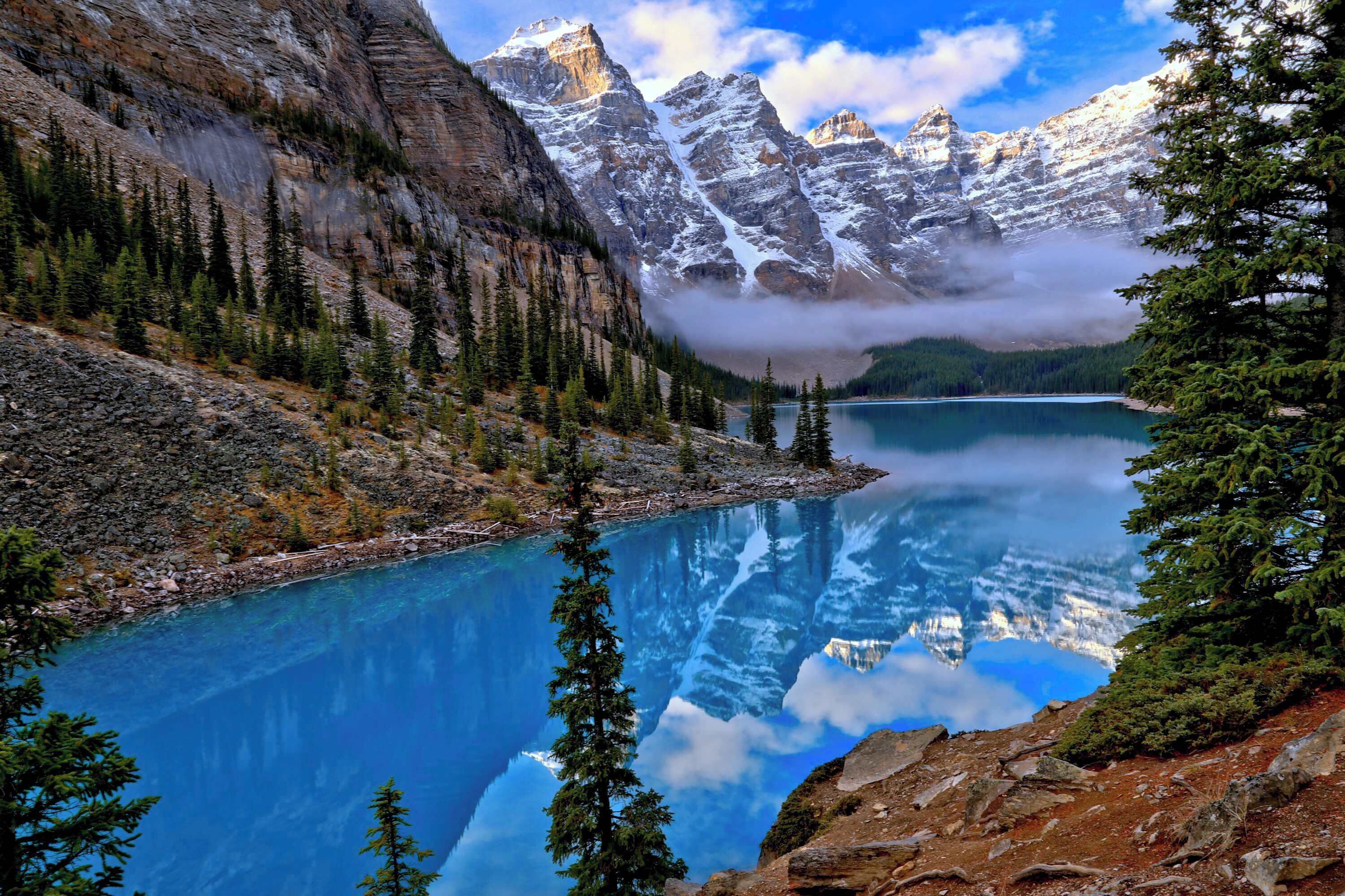 A mountain lake with clear reflections, surrounded by rocky terrain and evergreen trees.