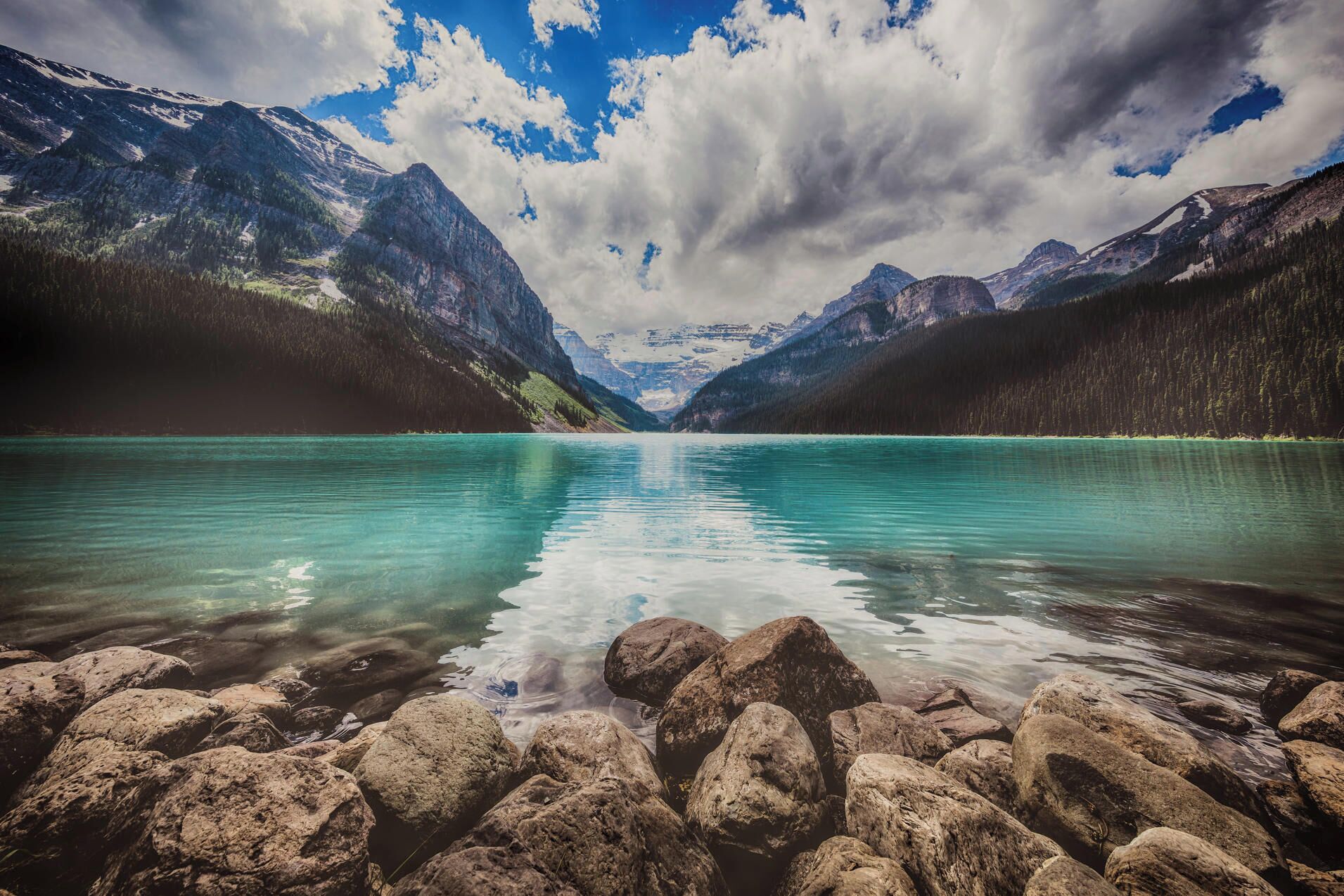 A lake with mountains in the background, clear water, and rocks in the foreground.