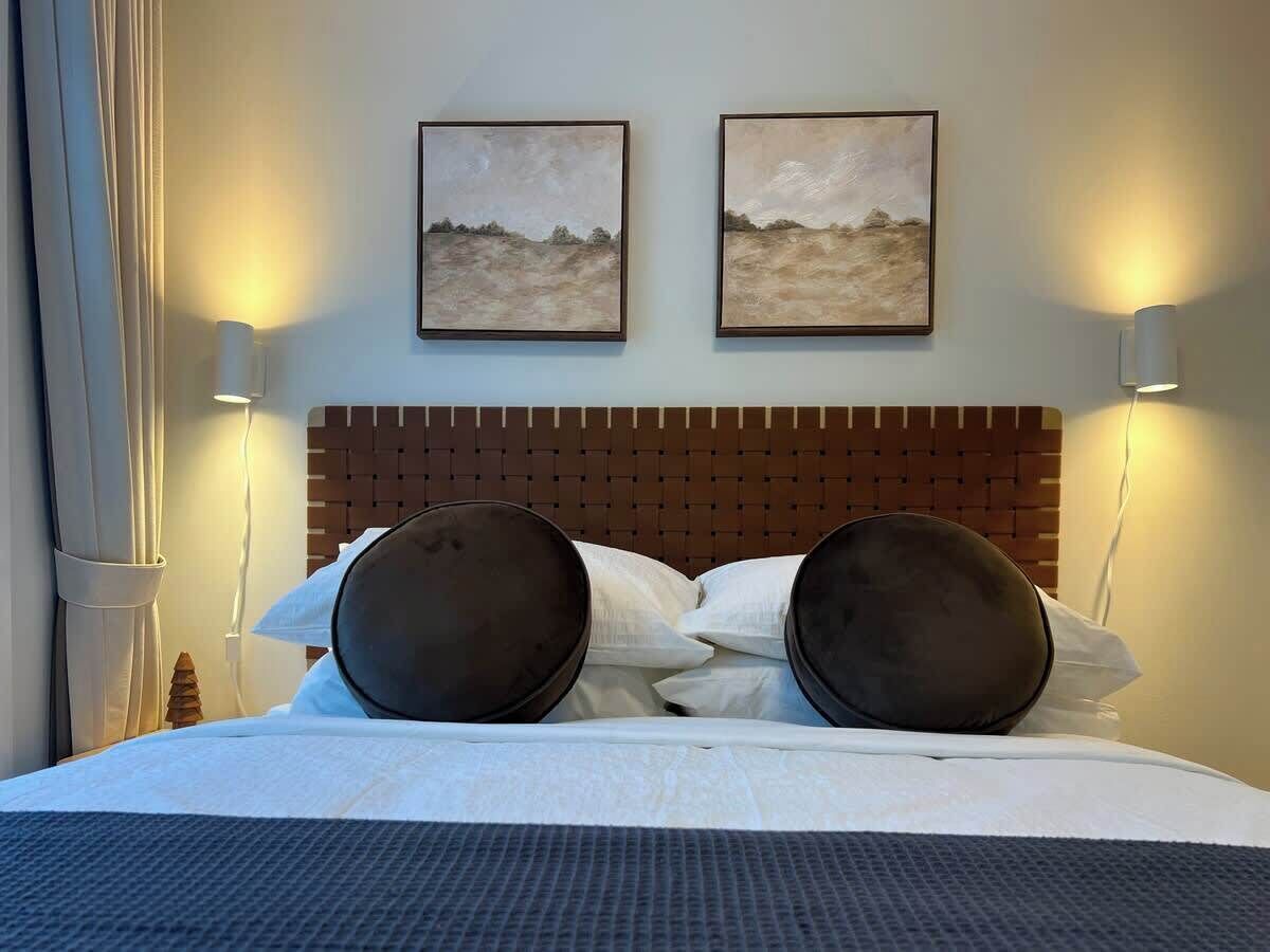 A hotel room with a large bed, two wall-mounted paintings, and two bedside lamps.