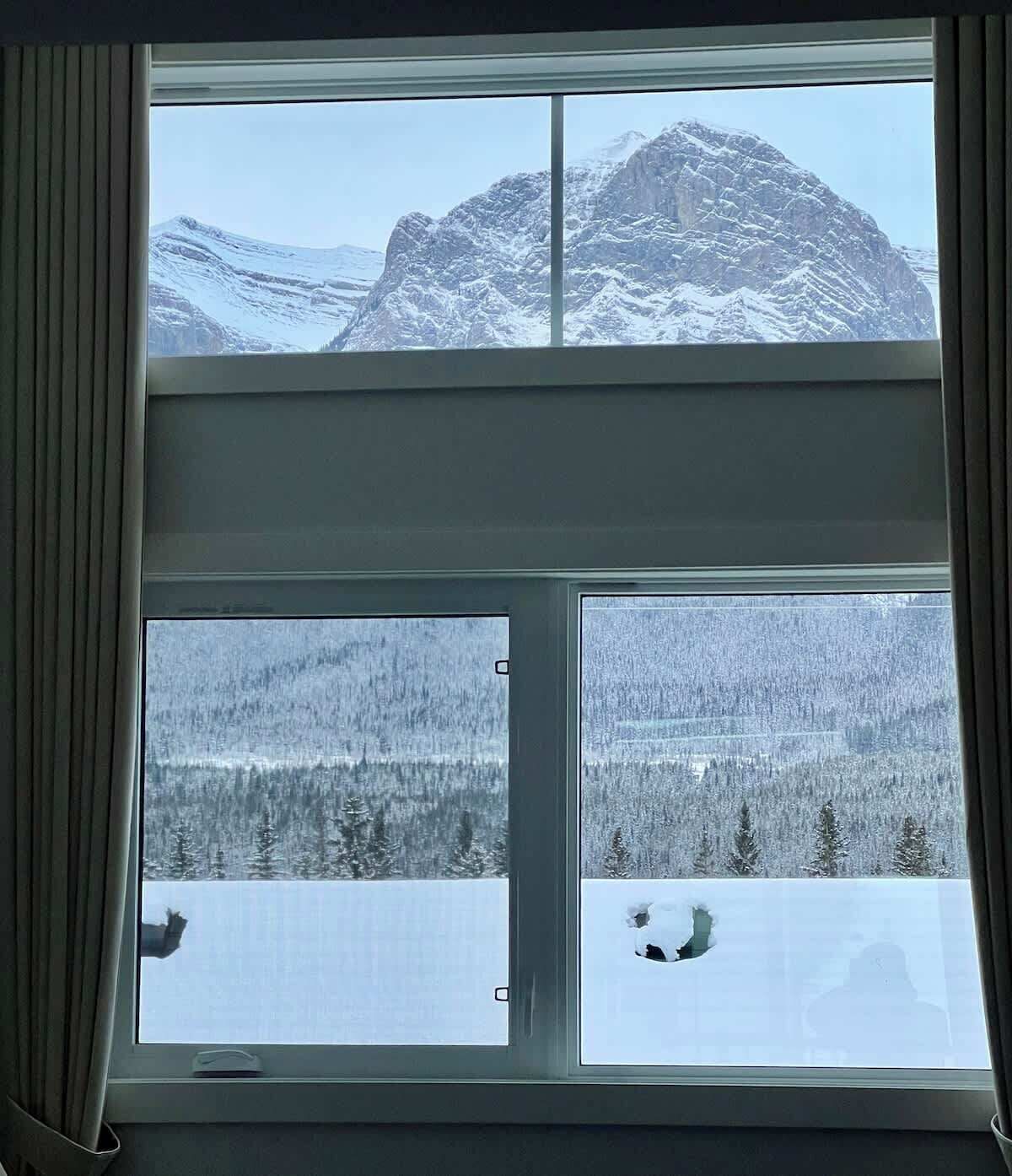 A window with a view of snow-covered mountains and a forest.