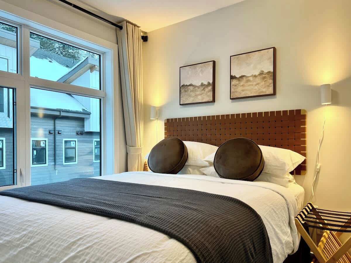 Hotelkamer met een groot bed, twee aan de muur bevestigde schilderijen, een houten hoofdeinde en uitzicht op een gebouw.