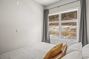 A bedroom with a bed, a window with curtains, and a view of a snowy landscape.
