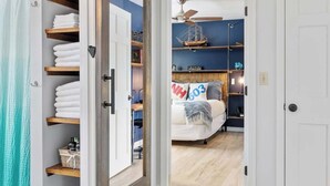A bedroom with a bed, a nightstand, a shelf with decorative items, and a wardrobe with folded towels. - "Big Sky" Retreat Atop Sunapee / Ski + Lake Life (Newbury)
