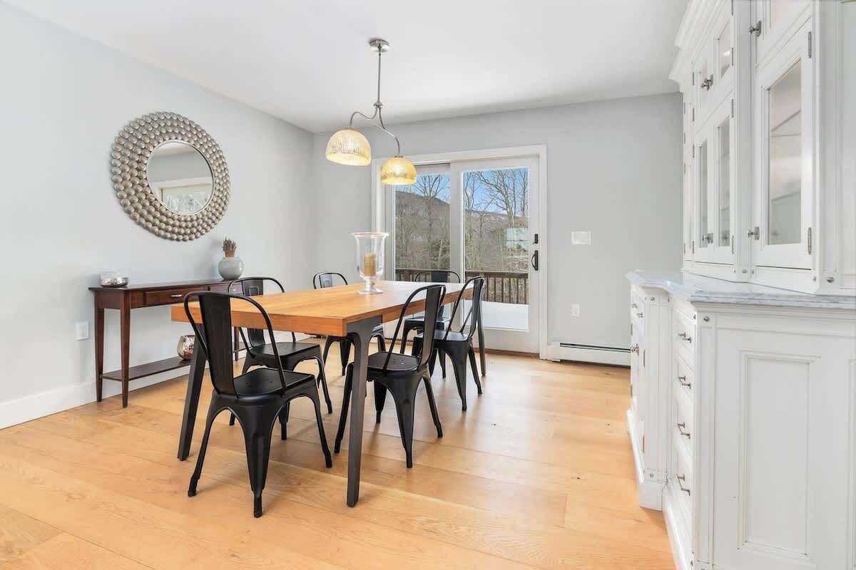 Un coin repas avec une table en bois et des chaises noires, un miroir rond accroché au mur et une vue à travers une porte vitrée.