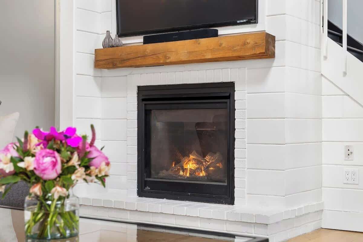Una chimenea con un televisor encima, un estante de madera y un florero con flores.
