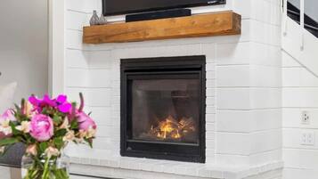 Una chimenea con un televisor encima, un estante de madera y un florero con flores.