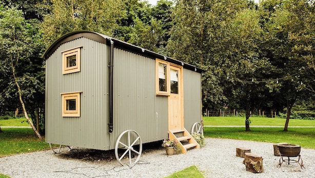 A small, single-story cabin with a door, windows, and a wheelbarrow.