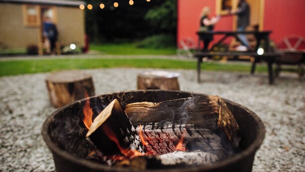 A campfire with logs and flames, a picnic table, and a building with a red exterior in the background. - Cosy en suite shepherd hut on the grounds of Historic building Samlesbury Hall (Samlesbury)