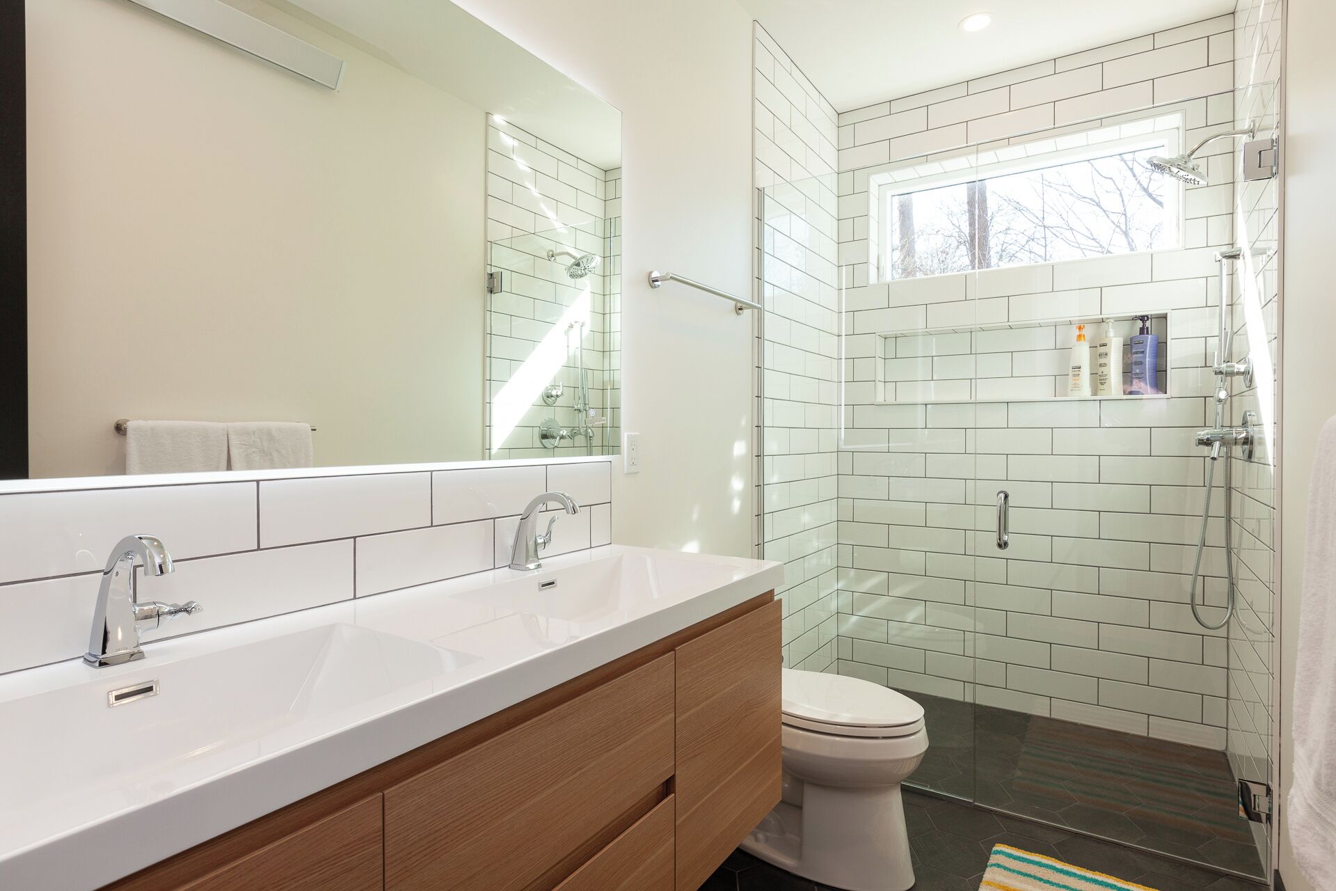 A modern bathroom with a large mirror, two sinks, a toilet, and a glass-enclosed shower area.