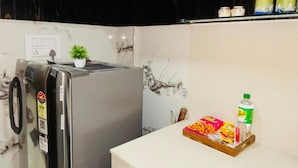 Eine Küche mit dunklen Holfschränken, einem Edelstahl-Kühlschrank, einer weißen Arbeitsplatte und einem kleinen Blumentopf.