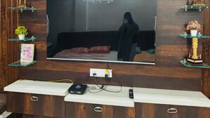 Ein Wohnzimmer mit einem großen Flachbildfernseher an einer Holzwand, einem marmorierten Boden und einem weißen Konsolentisch mit elektronischen Geräten.