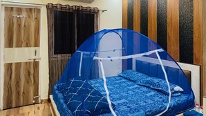 Ein Schlafzimmer mit einem Bett, das mit einem blauen Baldachin bedeckt ist, Holzboden und einem Deckenventilator.
