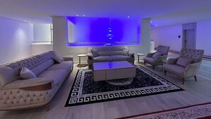 Een moderne woonkamer met een grote flatscreen televisie, een zithoek, een salontafel en een vloerkleed met een patroon.