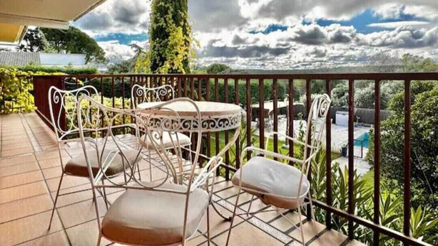 A balcony with a table and chairs, overlooking a garden and a swimming pool. - 7picos-the house in Galapagar. Villa with swimming pool, ideal for family vacations. (Galapagar)