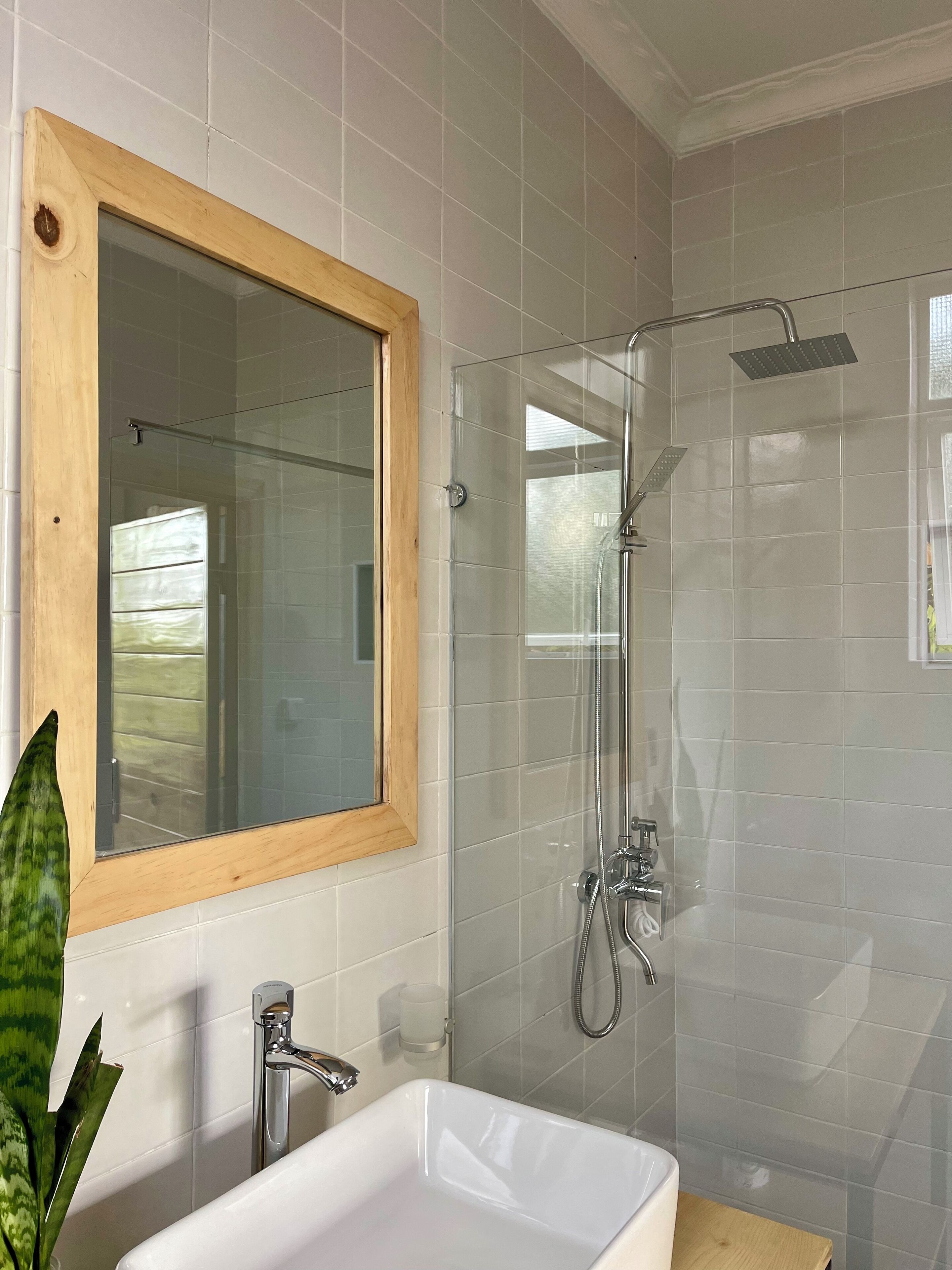 A bathroom with a glass-enclosed shower, a wooden-framed mirror, and a white sink.