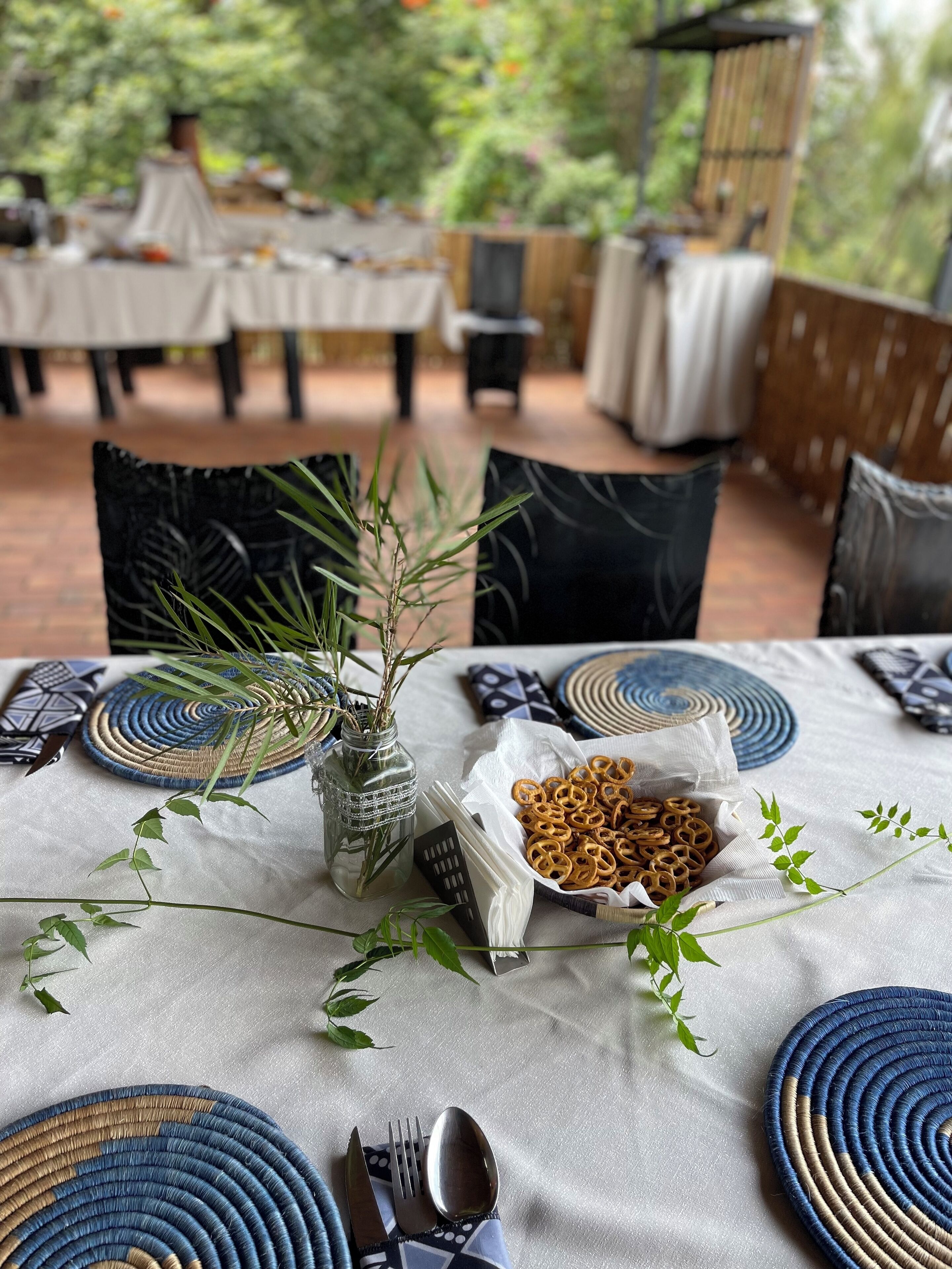 An outdoor dining area with round woven placemats, a bowl of pretzels, and a small vase with a plant.