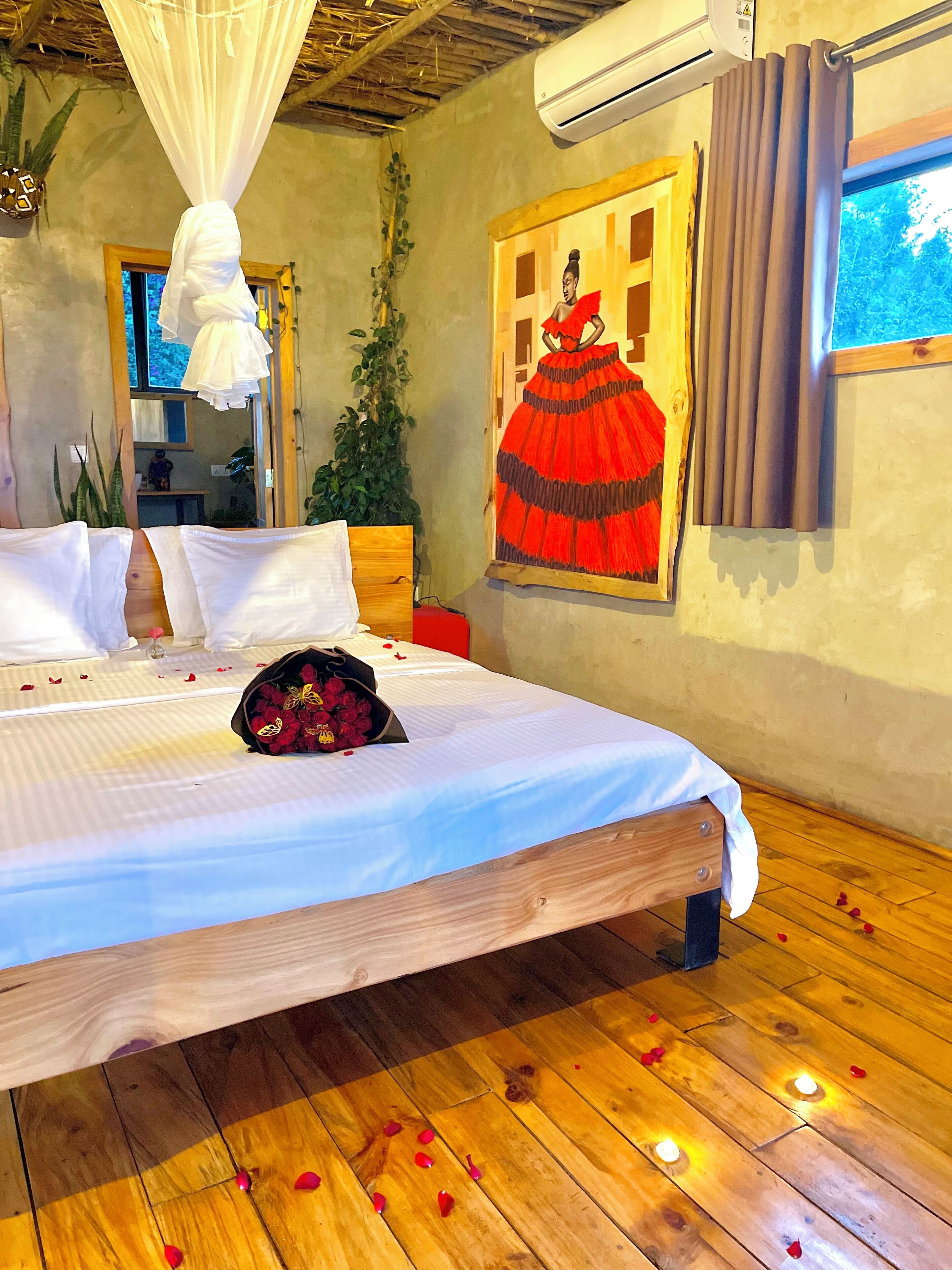 Una cama bien hecha con sábanas blancas, un ramo de flores rojas y pétalos de rosa esparcidos sobre el suelo de madera.