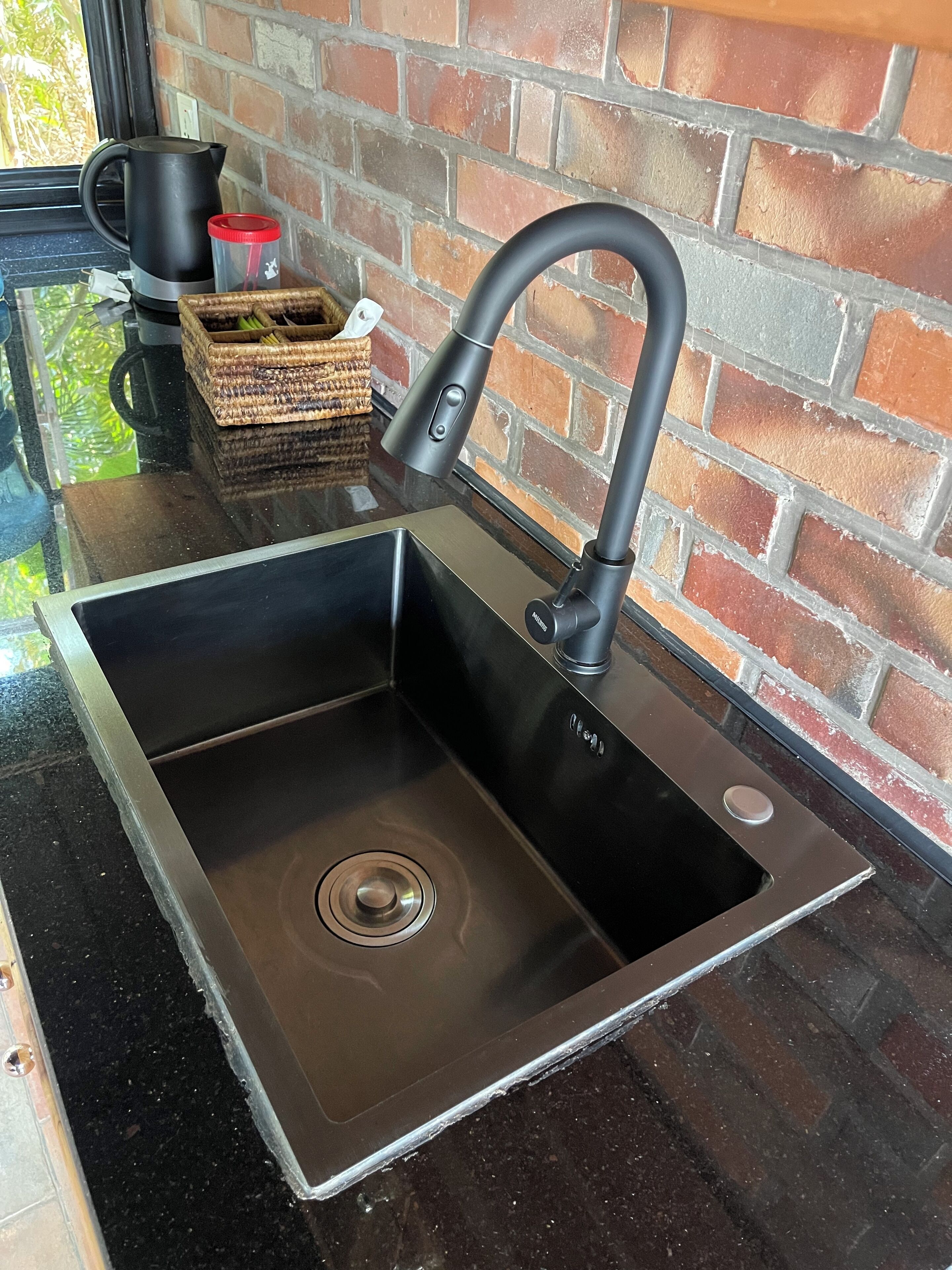 Cocina moderna con un lavamanos de acero inoxidable, un grifo negro y un fondo de pared de ladrillo.