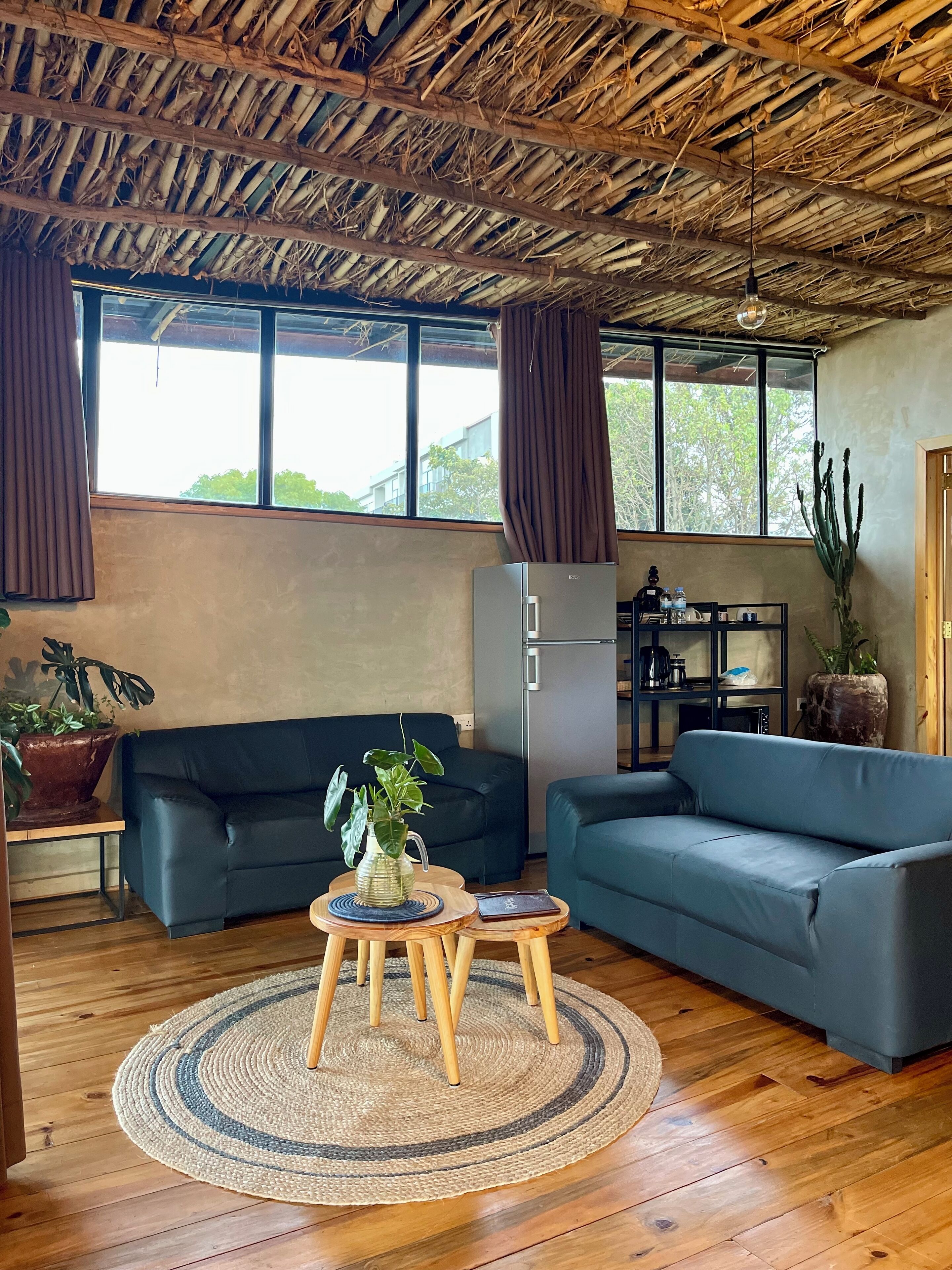 A living room with a thatched roof, two sofas, a coffee table, and a refrigerator.