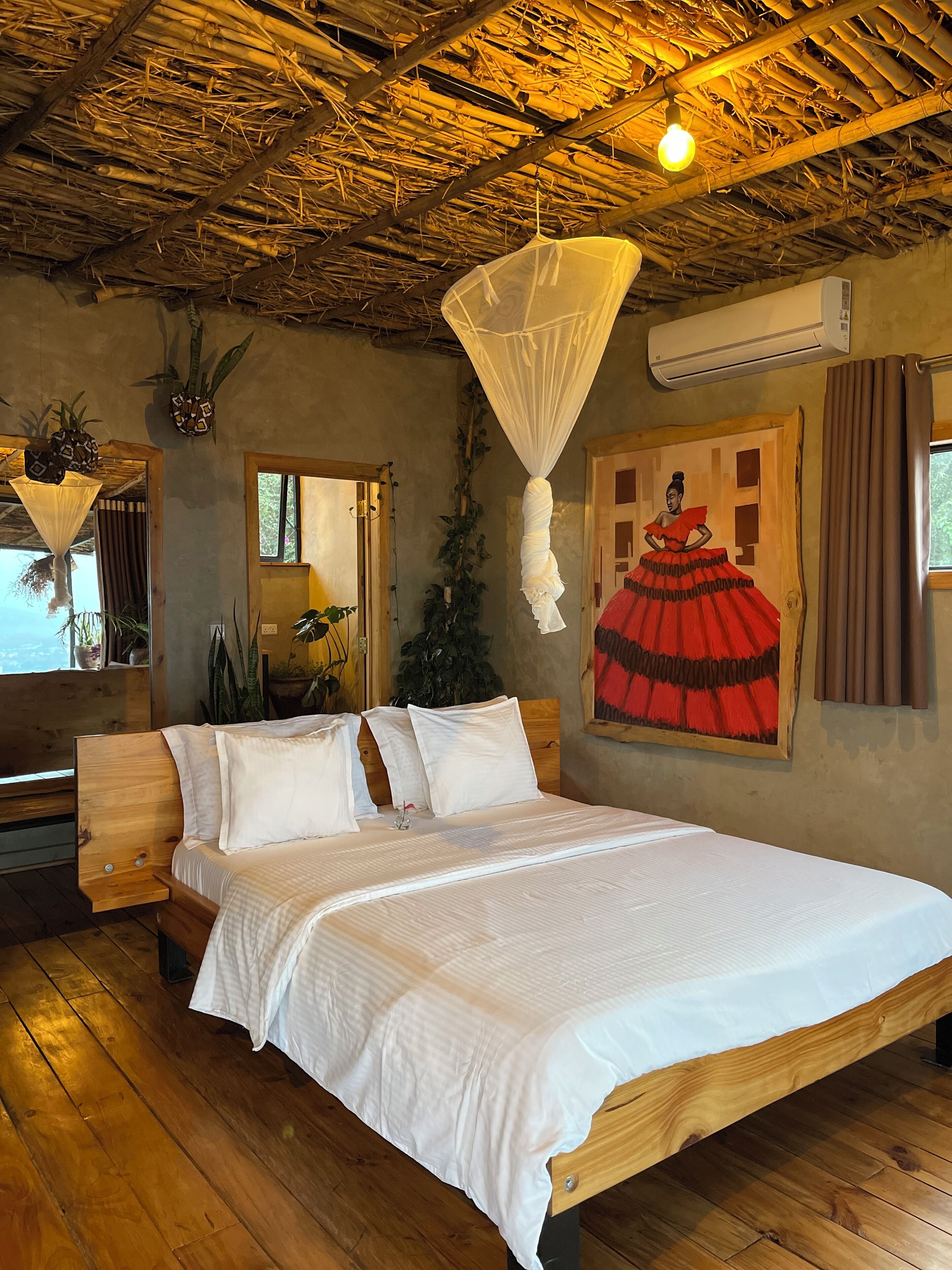 A wooden bed with white bedding, a mosquito net, and a painting of a woman in a red dress on the wall.