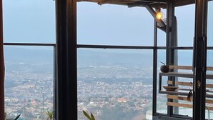 A modern kitchen with a wooden countertop, a hanging light fixture, and a view of the city through large windows. - Eagle View Lodge (Kigali)