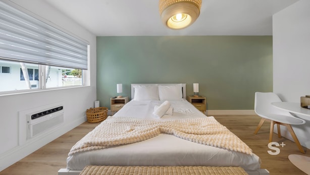 Ein modernes Schlafzimmer mit einem großen Bett, Nachttischen, einem Korbstuhl und einer Hängeleuchte.