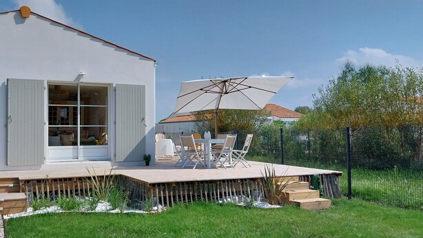 A white house with a wooden deck, a dining set, and a large umbrella.