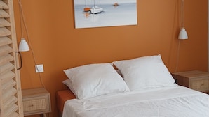 A bedroom with a bed, a painting of sailboats, and a hanging light fixture.